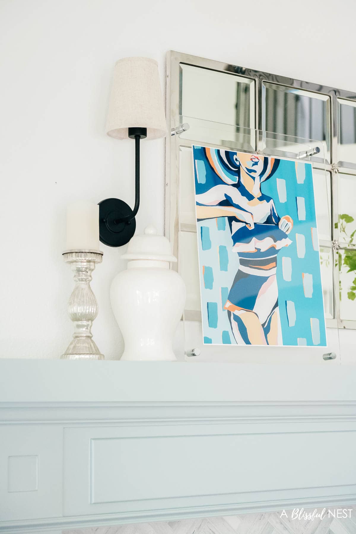 bathing suit artwork in a lucite frame with a white ginger jar and mercury glass candlestick on a mantel.