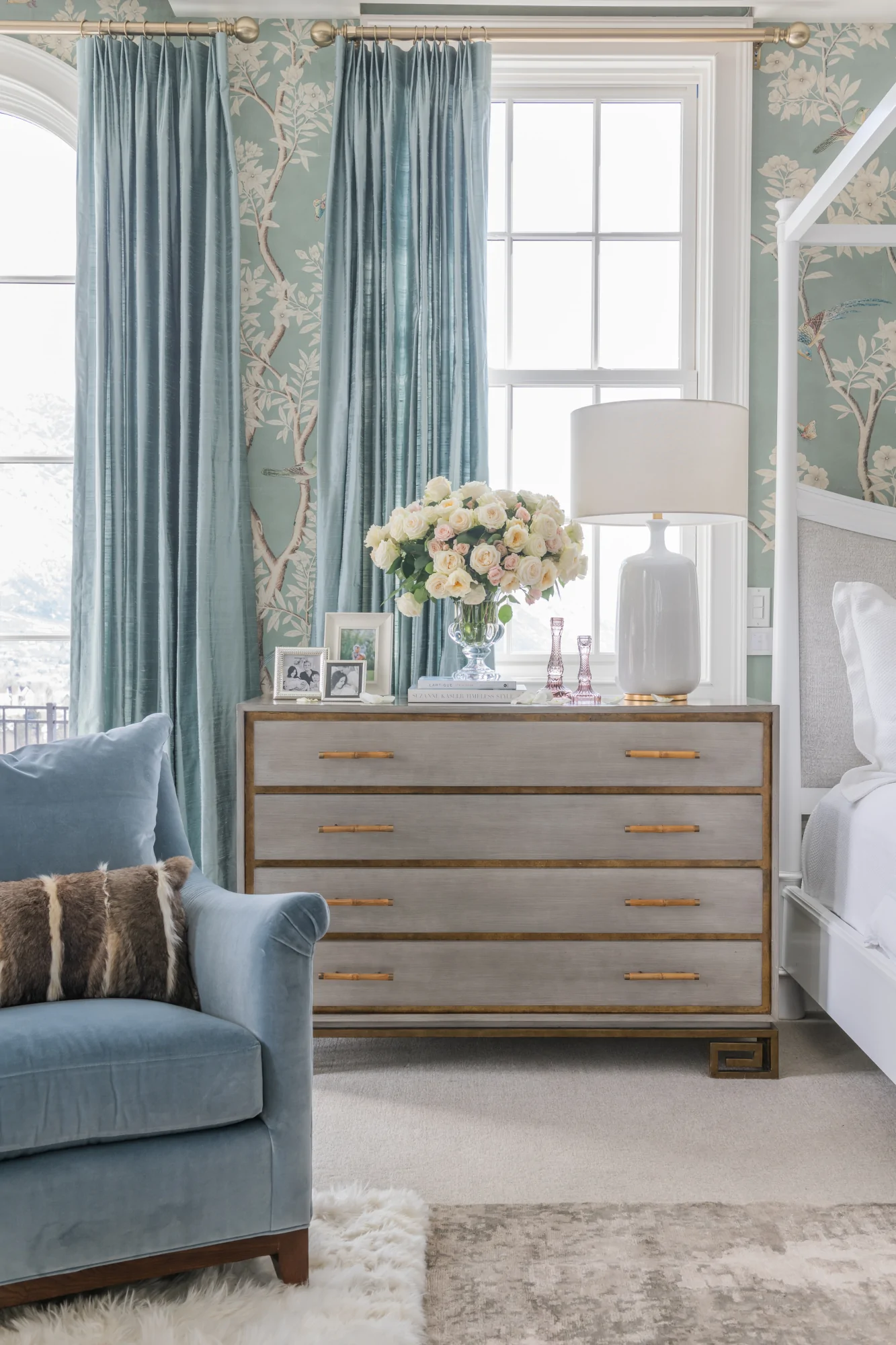 Soft aqua drapes and matching patterned wallpaper with a grey nightstand with white table lamp.