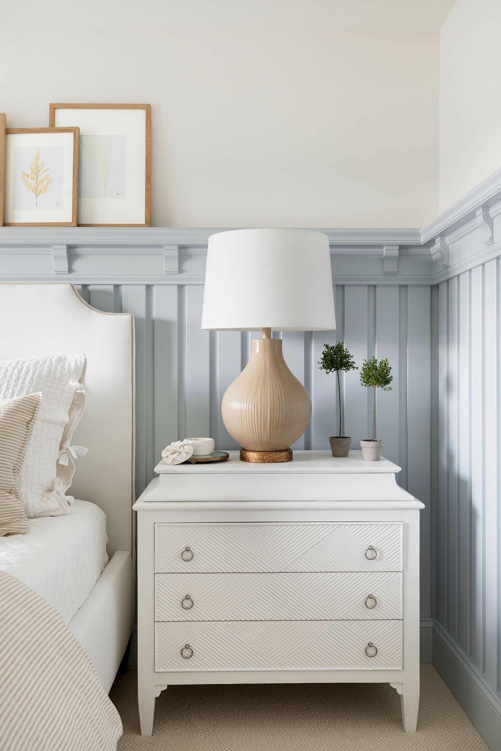 Pale blue board and batten wall treatment with a white nightstand and tan colored table lamp. 