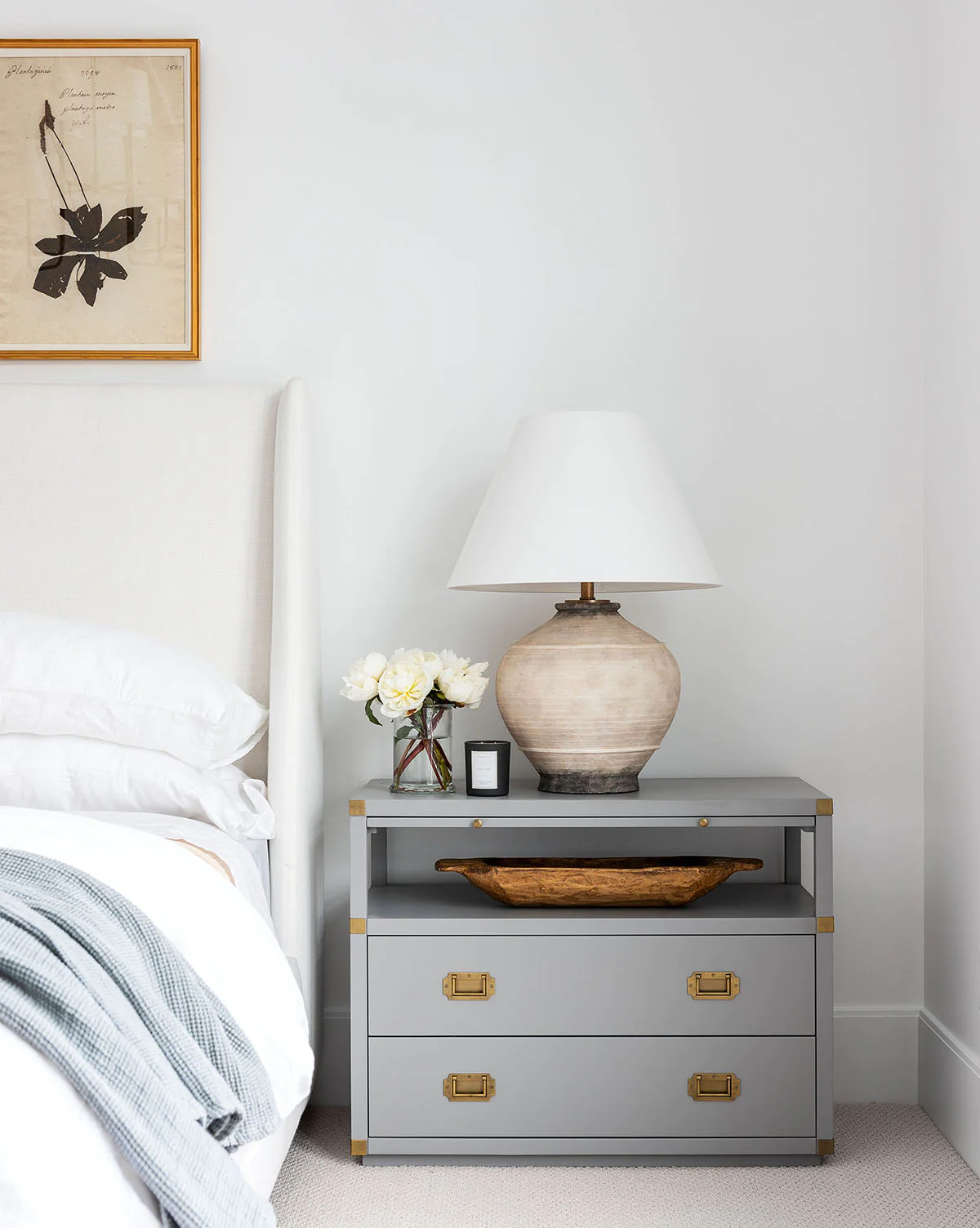 Grey blue nightstand with a earthenware table lamp and white faux peonies in vase. 