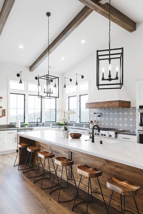 Black pendant lanterns, warm wood toned kitchen island, marble kitchen counter, industrial wood barstools, black and white patterned tile