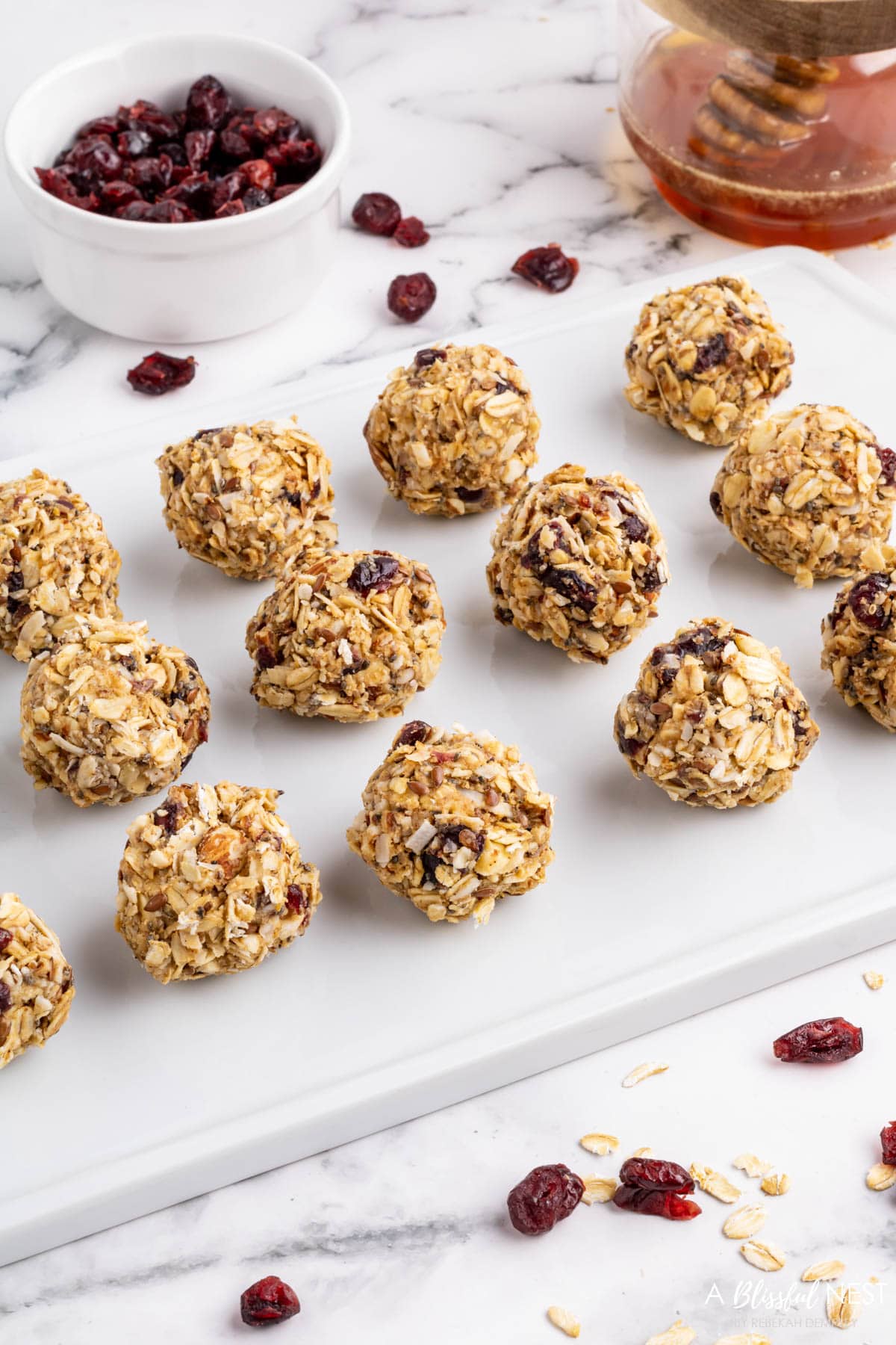 Energy balls lined up on a white cutting board. Including a bowl of cranberries.