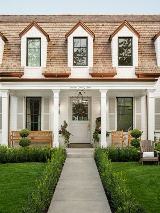 White painted brick, brown shingle roof, front door in a soft cream grey color. cedar benches on front porch.
