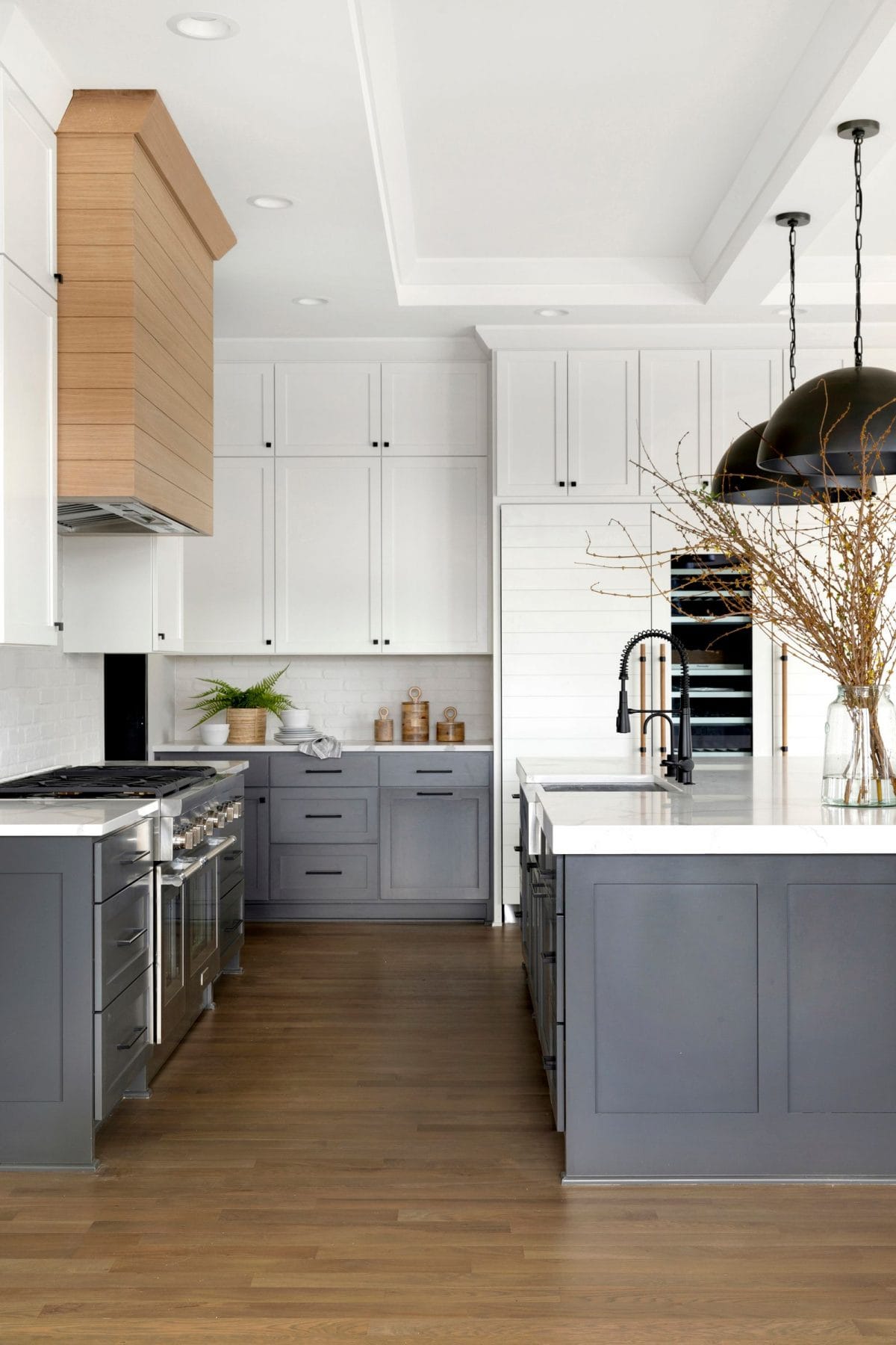 dark blue gray lower kitchen cabinets, white upper kitchen cabinets, black cabinet hardware, natural wood shiplap range hood.