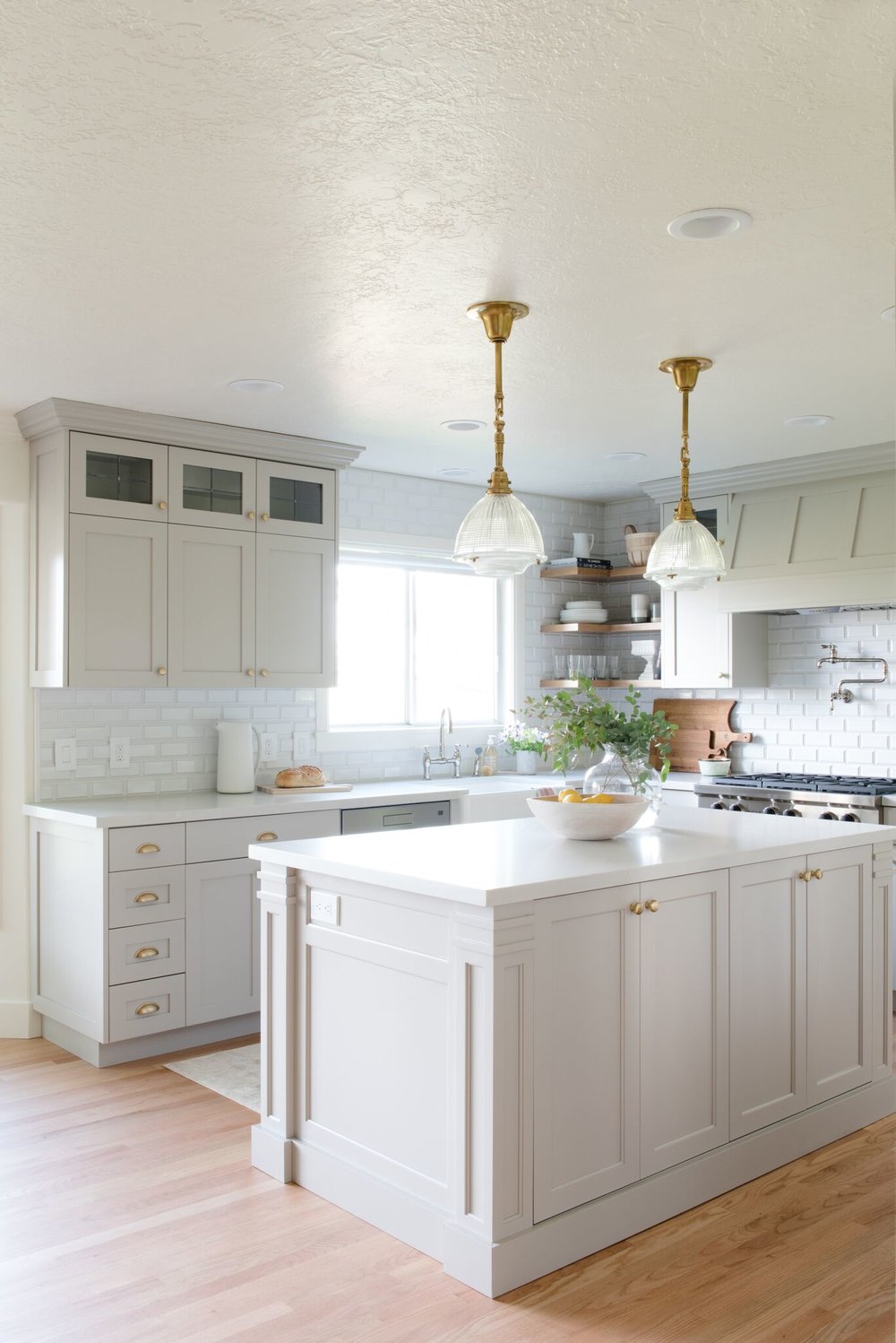 light grey kitchen cabinets with gold hardware, white quartz countertops, white subway tile backsplash