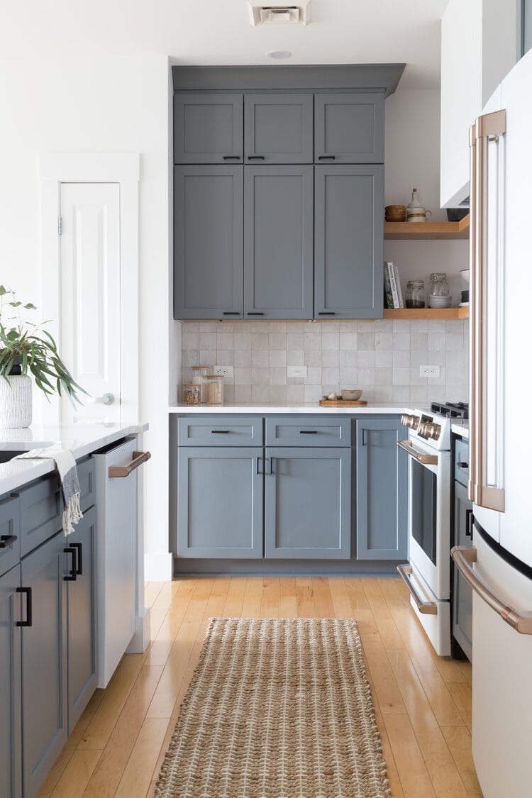 dark blue gray cabinet color with black hardware, honey oak flooring, and white painted walls