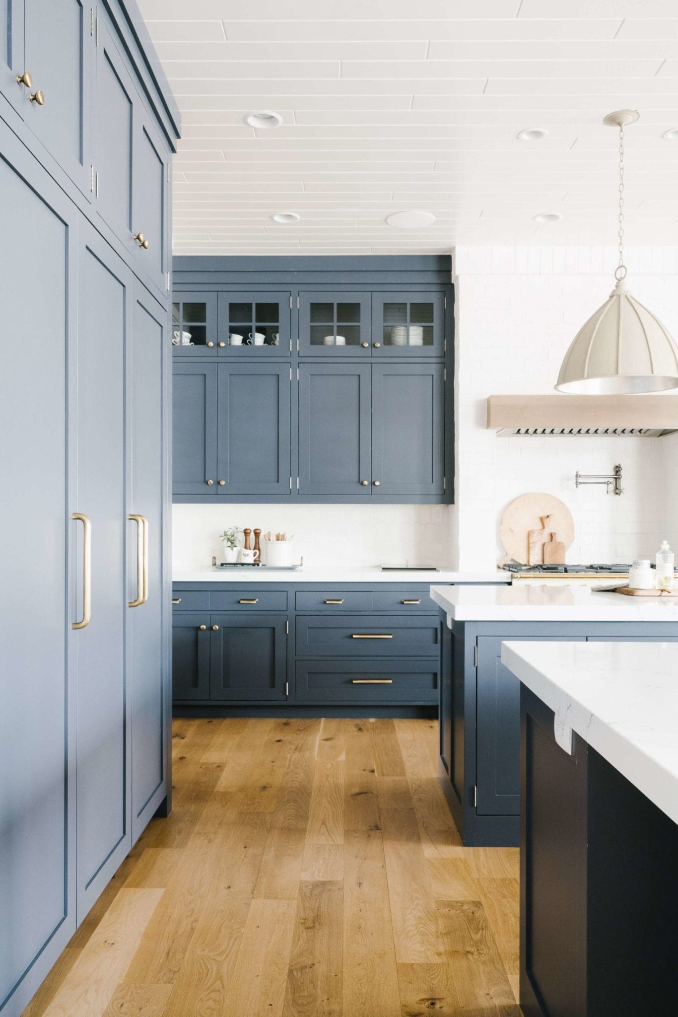 Blue gray kitchen cabinets with oak flooring, gold cabinet hardware.