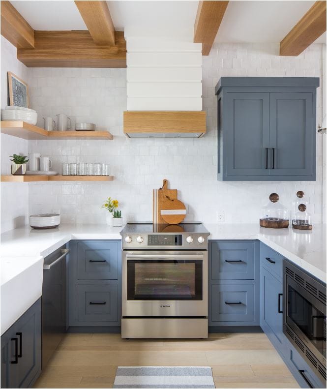 Rich deep blue kitchen cabinets with black hardware, wood floating shelves, white shiplap hood with wood detail