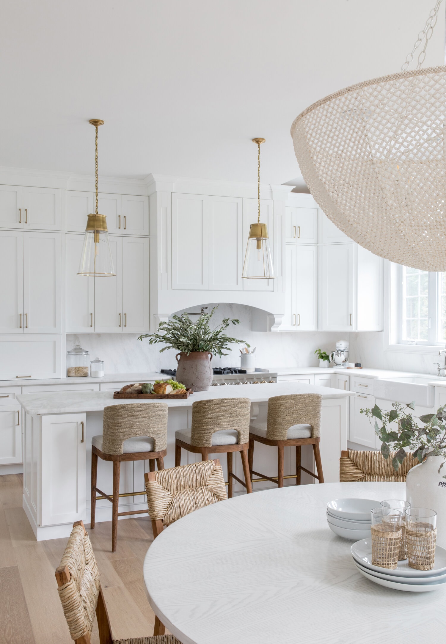 All white kitchen using barstools and chairs to add texture to the room in seagrass and jute. Gold lighting and hardware.
