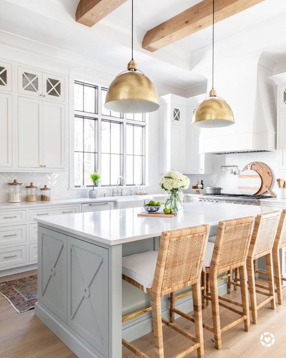 Light grey kitchen island with gold dome pendant lights, rattan barstools, white kitchen cabinets