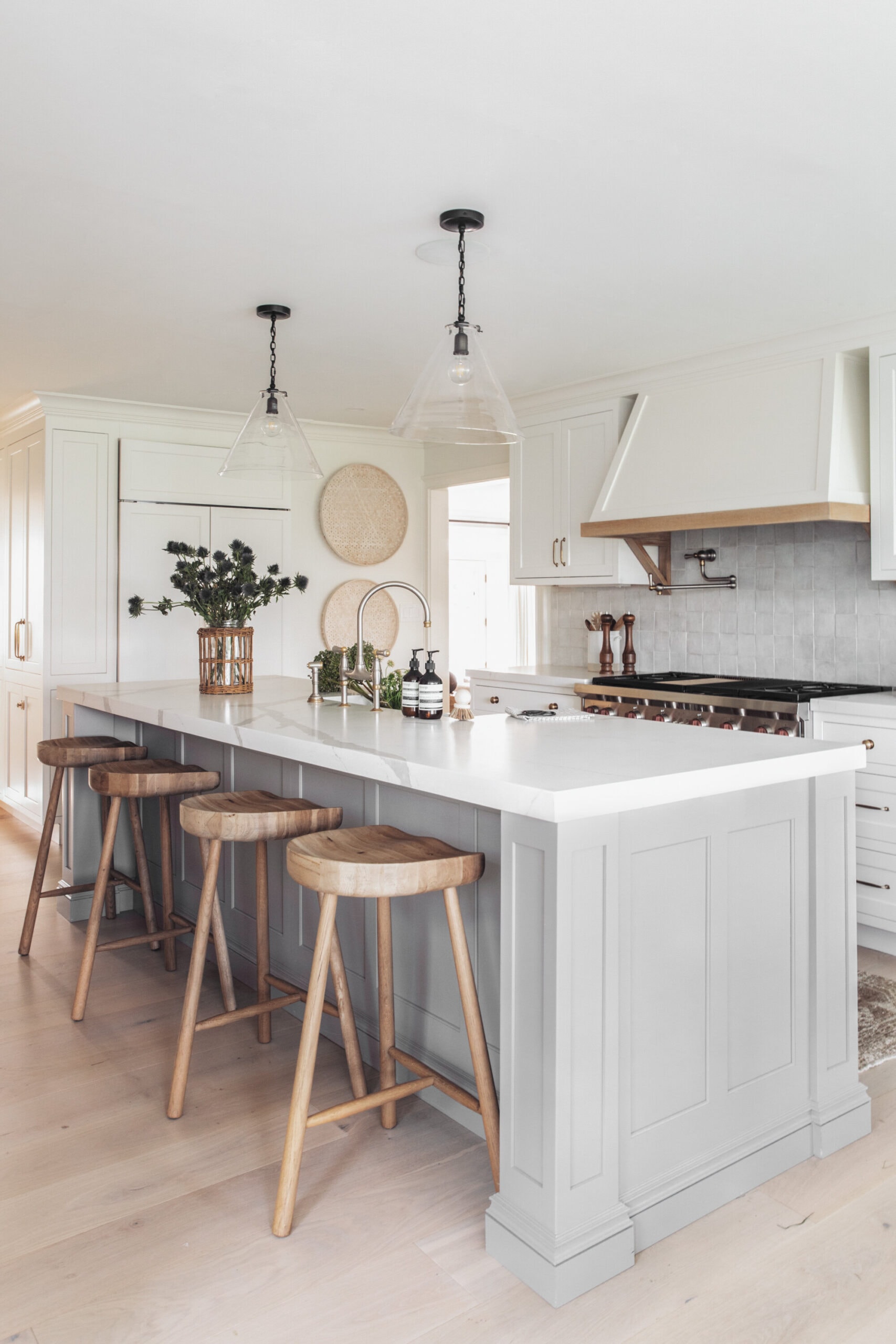 light grey kitchen island, white kitchen cabinets, wood industrial barstools, glass pendant lights over island