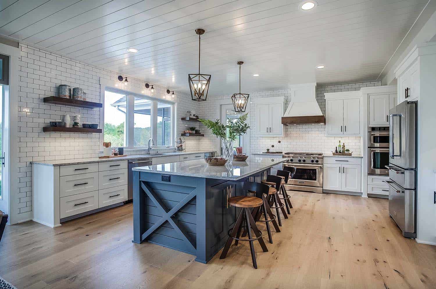 blue kitchen island with white wood cabinets, wood detail on range hood, pine floors, oil rubbed bronze lantern pendant lights about island