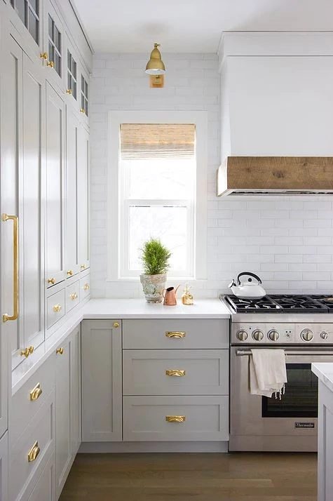 Medium gray kitchen cabinets with a white range hood with rustic wood accent and gold cabinet hardware.