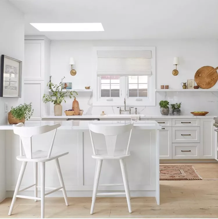 all white kitchen cabinets and light wood floors. window over kitchen sink, floating white shelves