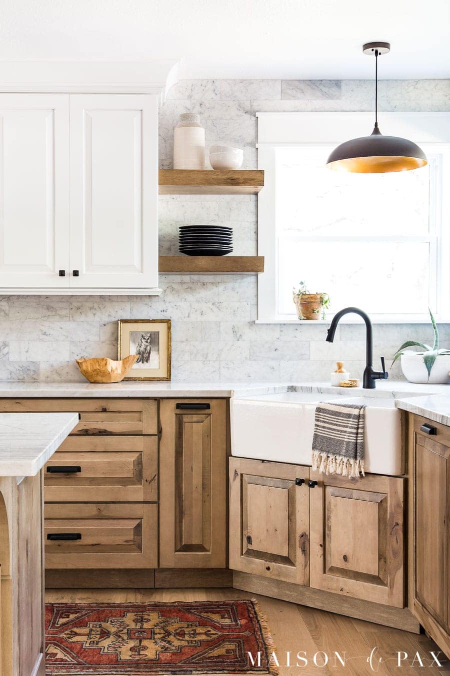 light wood lower cabinets with black hardware. white upper cabinets, farmhouse sink