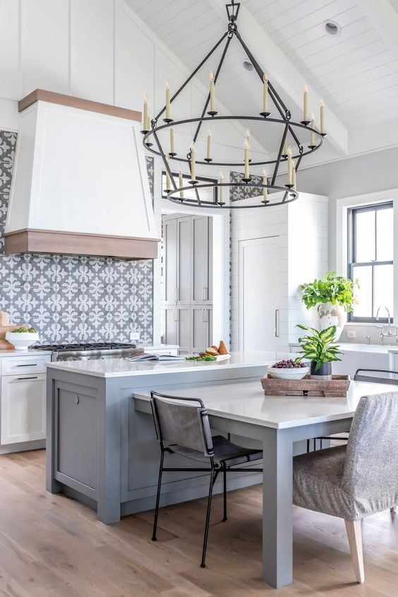 Light blue gray island with grey and white patterned backsplash tile, white kitchen cabinets. Wood accents on a white hood