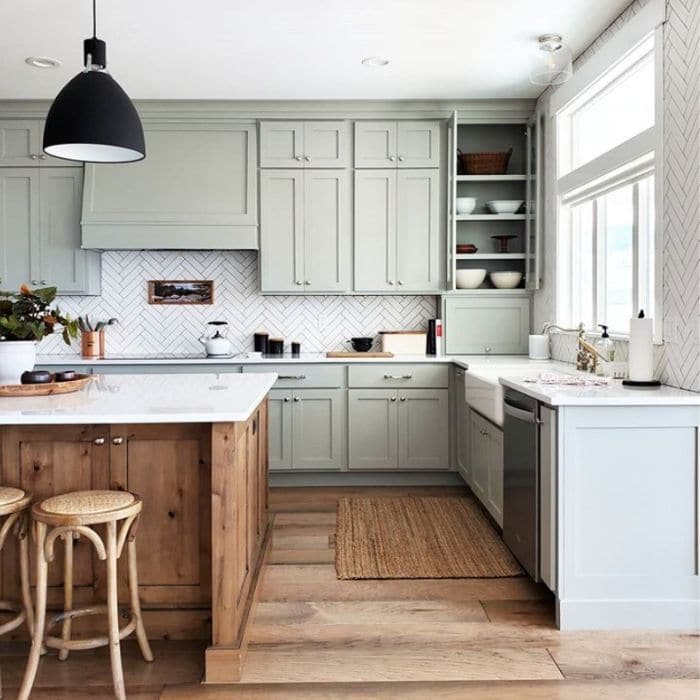 rustic wood kitchen island with sage green kitchen cabinets, black dome pendant lights, white farmhouse sink