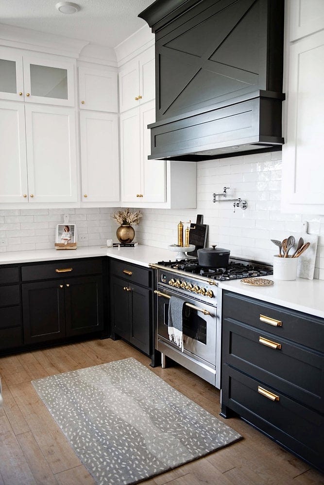 Black kitchen cabinets with white upper cabinets, marble countertops, and gold cabinet hardware