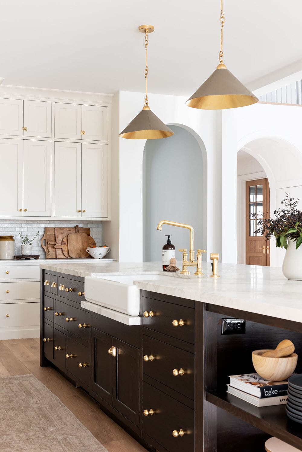Dark kitchen island with cream color cabinets and gold hardware.