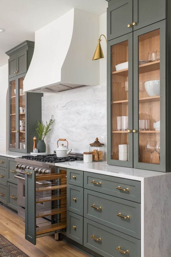 Dark green kitchen cabinetry, mixed with a modern white range hood and gold cabinet hardware