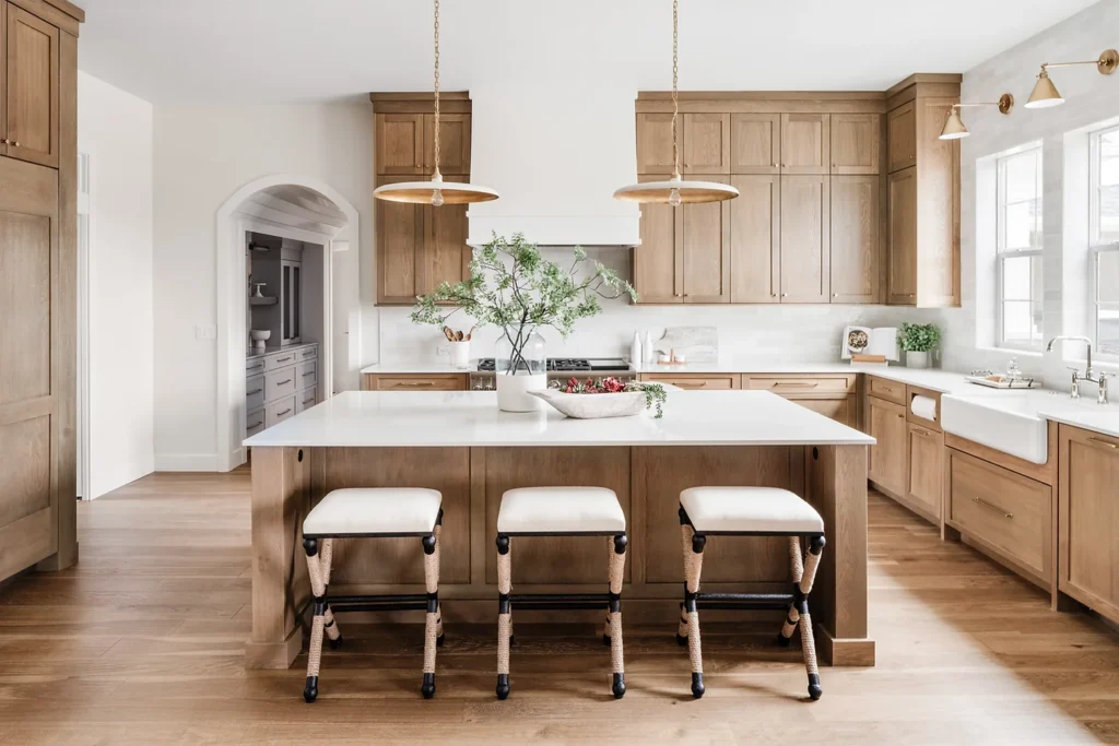 natural wood kitchen cabinets with white quartz countertops, gold pendant lights and sconces, white range hood