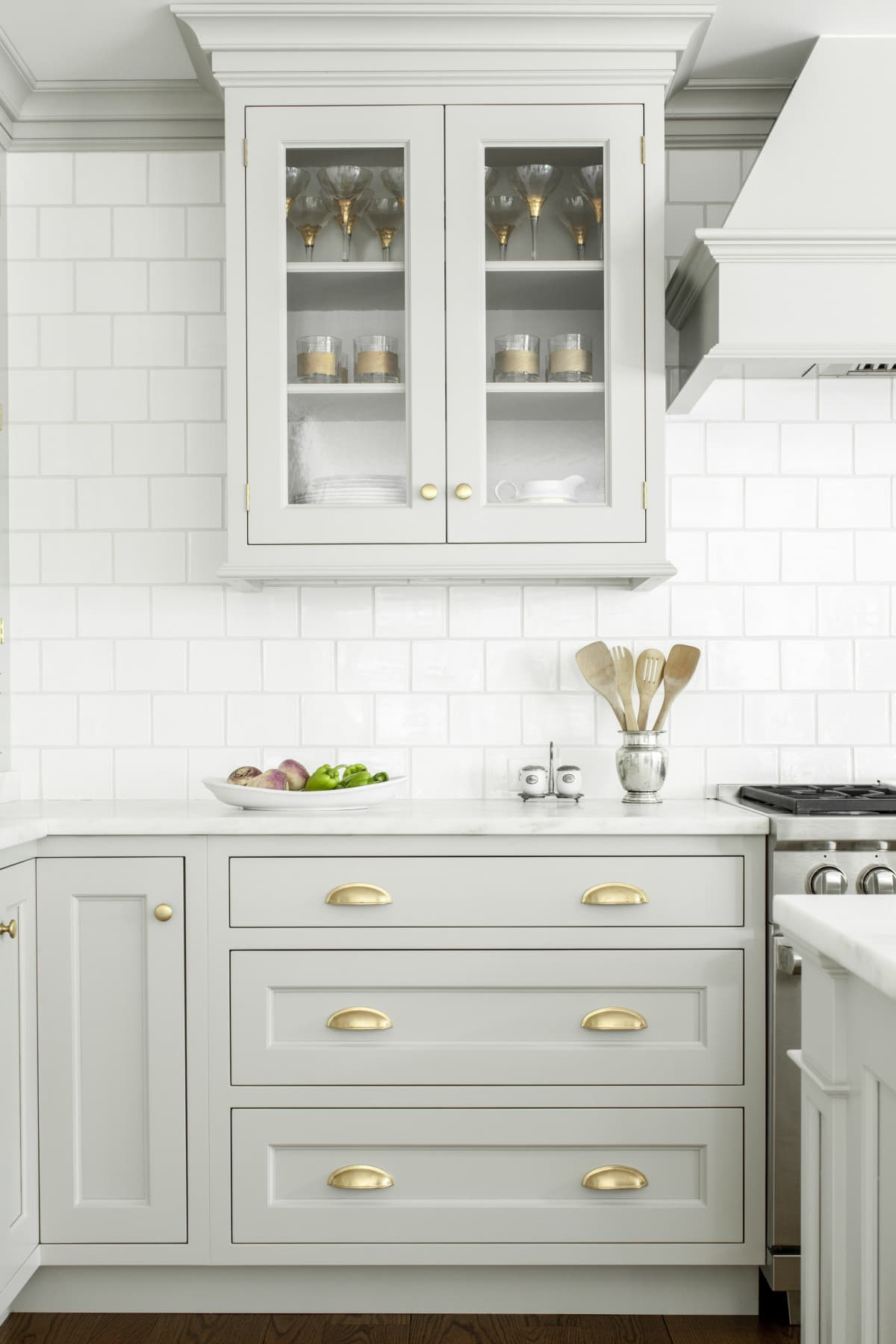 Light grey kitchen cabinets with a marble counter top and white subway tile backsplash, gold cabinet hardware