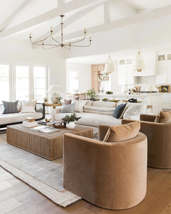 Tan velvet round club chairs in all creamy white living room and kitchen space. Aged brass lighting.