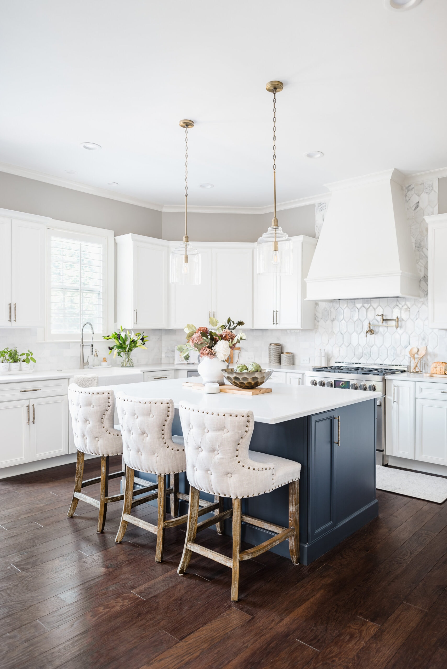White kitchen with navy island, upholstered barstools with tufting and nailheads