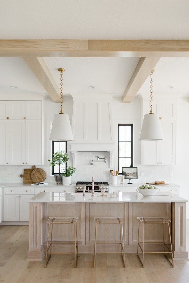 oak kitchen island with white and gold pendant lights, white cabinets and hood