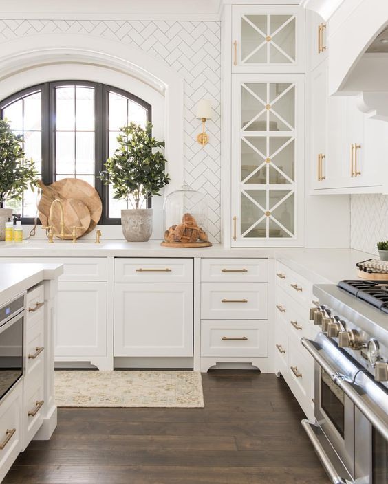 hexagon white tiles for backsplash with dark grout, white kitchen cabinets, gold cabinet hardware, dark wood flooring