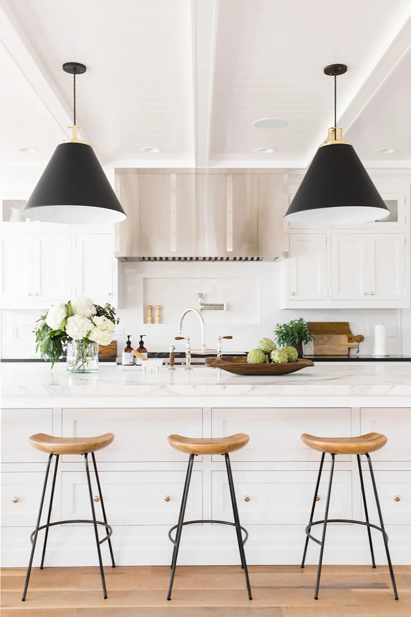 white kitchen cabinets mixed with black dome pendant lights, industrial wood barstools, oak flooring.