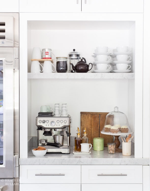 coffee station with floating shelf for storage, white coffee cups, cloche with cupcakes on a cake stand, espresso machine.