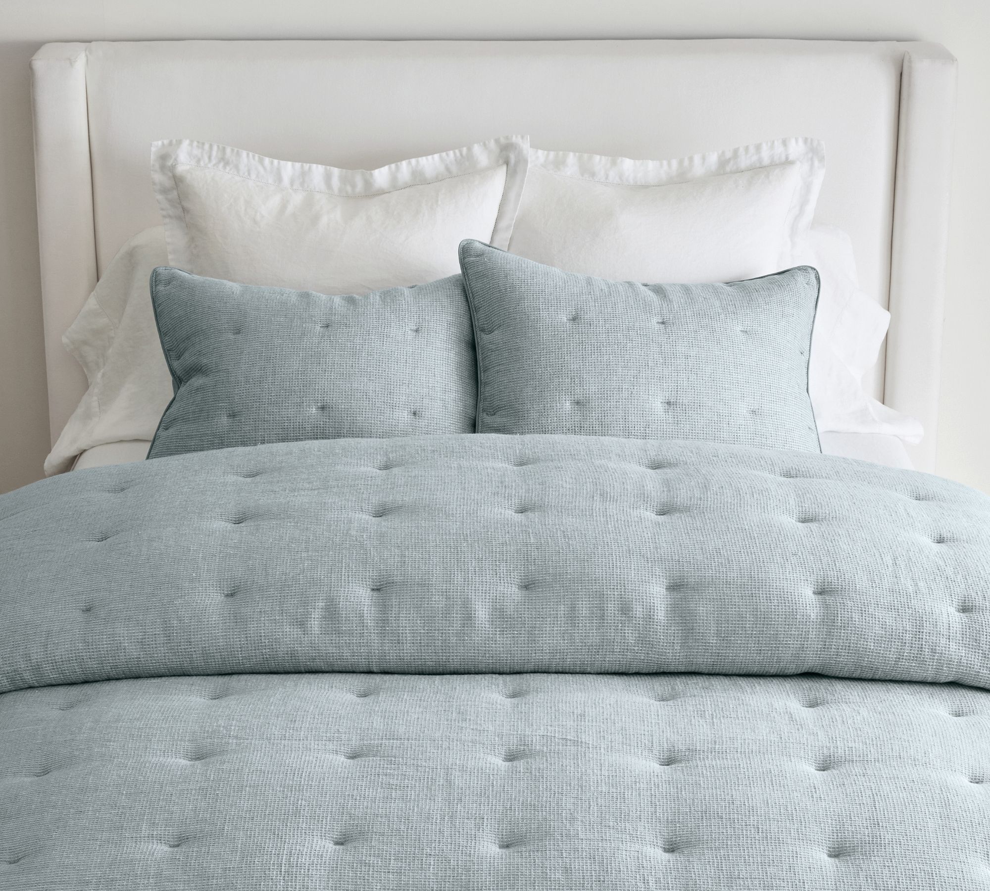 Light blue bedding set on a white upholstered bed.