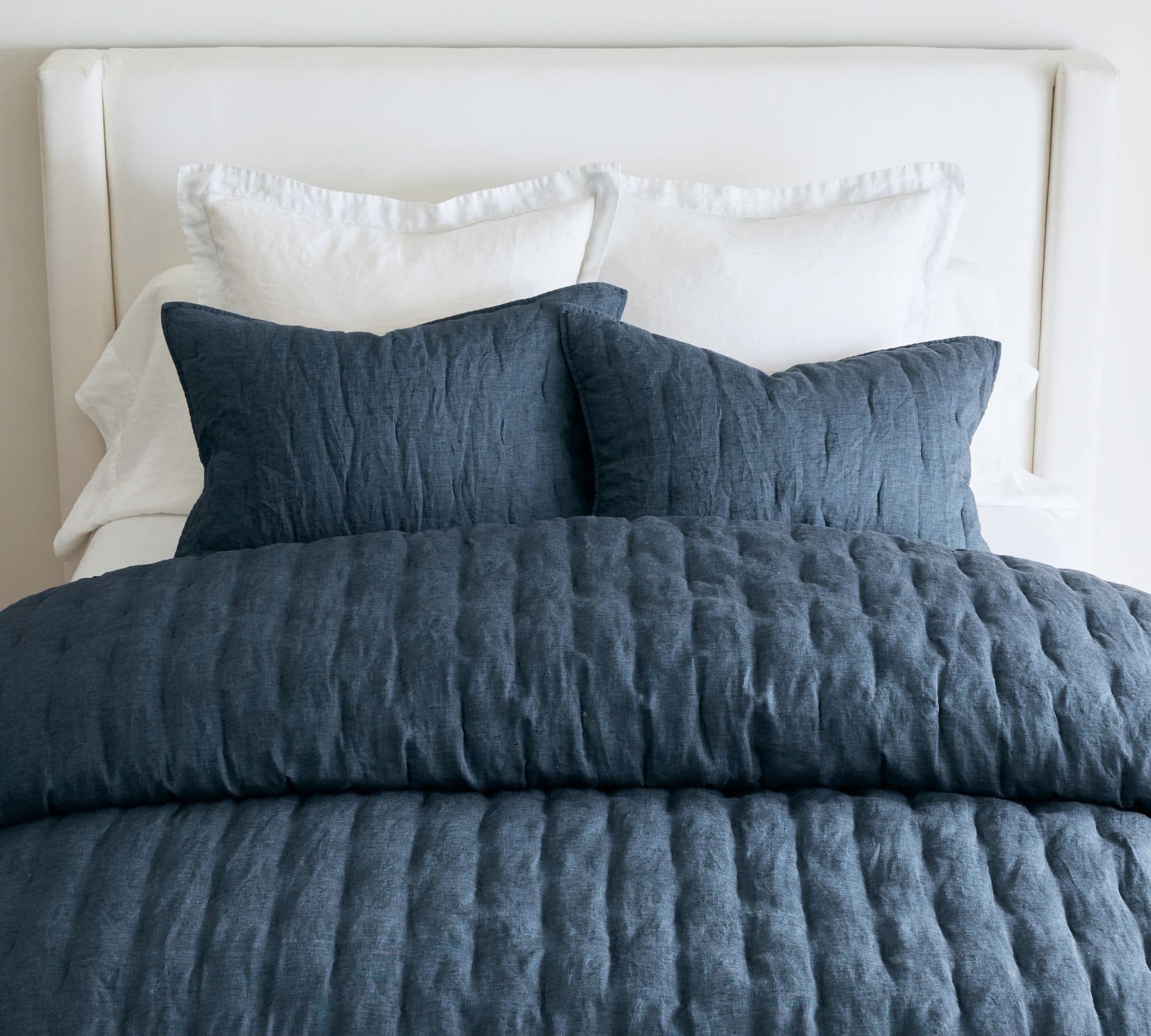 navy comforter and matching throw pillows on a white upholstered bed.