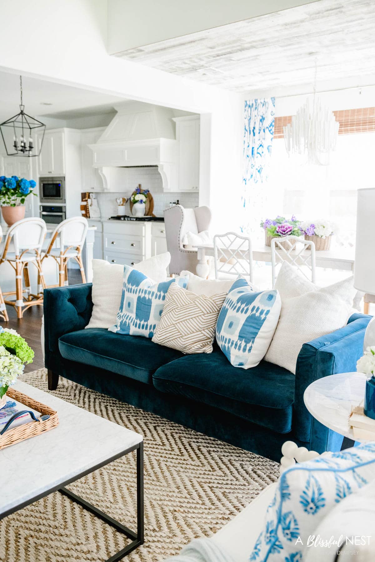 navy blue sofa in a white room with cream, blue, and rattan pillows on it.