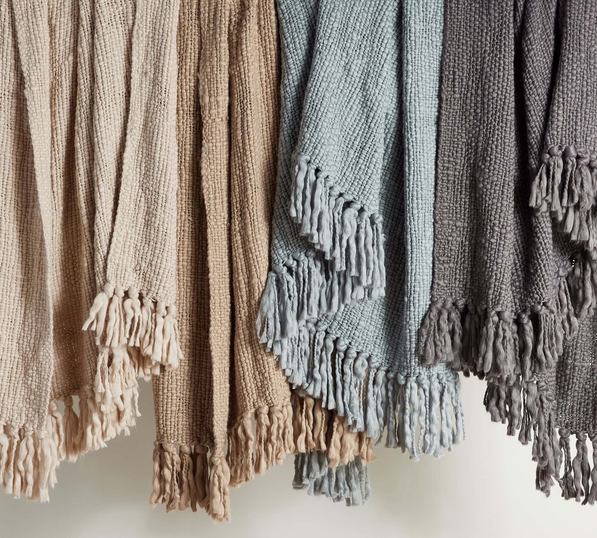 tassel throw blankets hanging in a row in cream, light blue, and dark grey