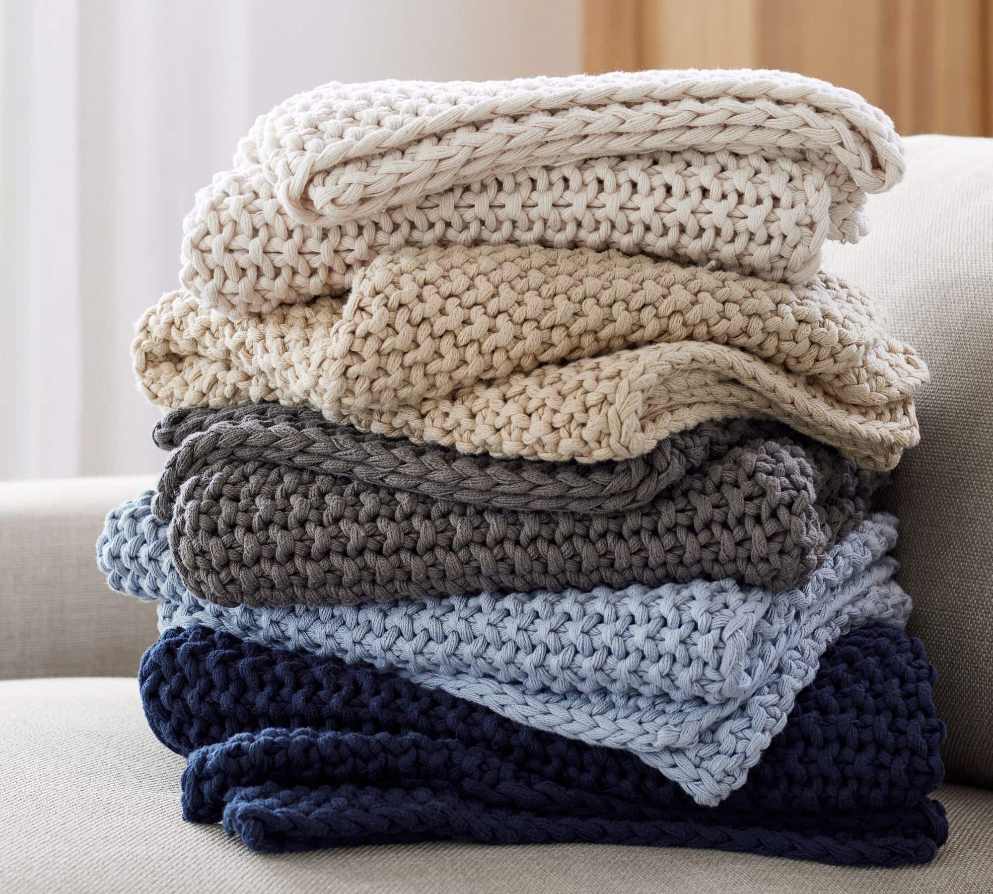 stack of chunky knit blankets in navy, blue, dark grey, and cream.