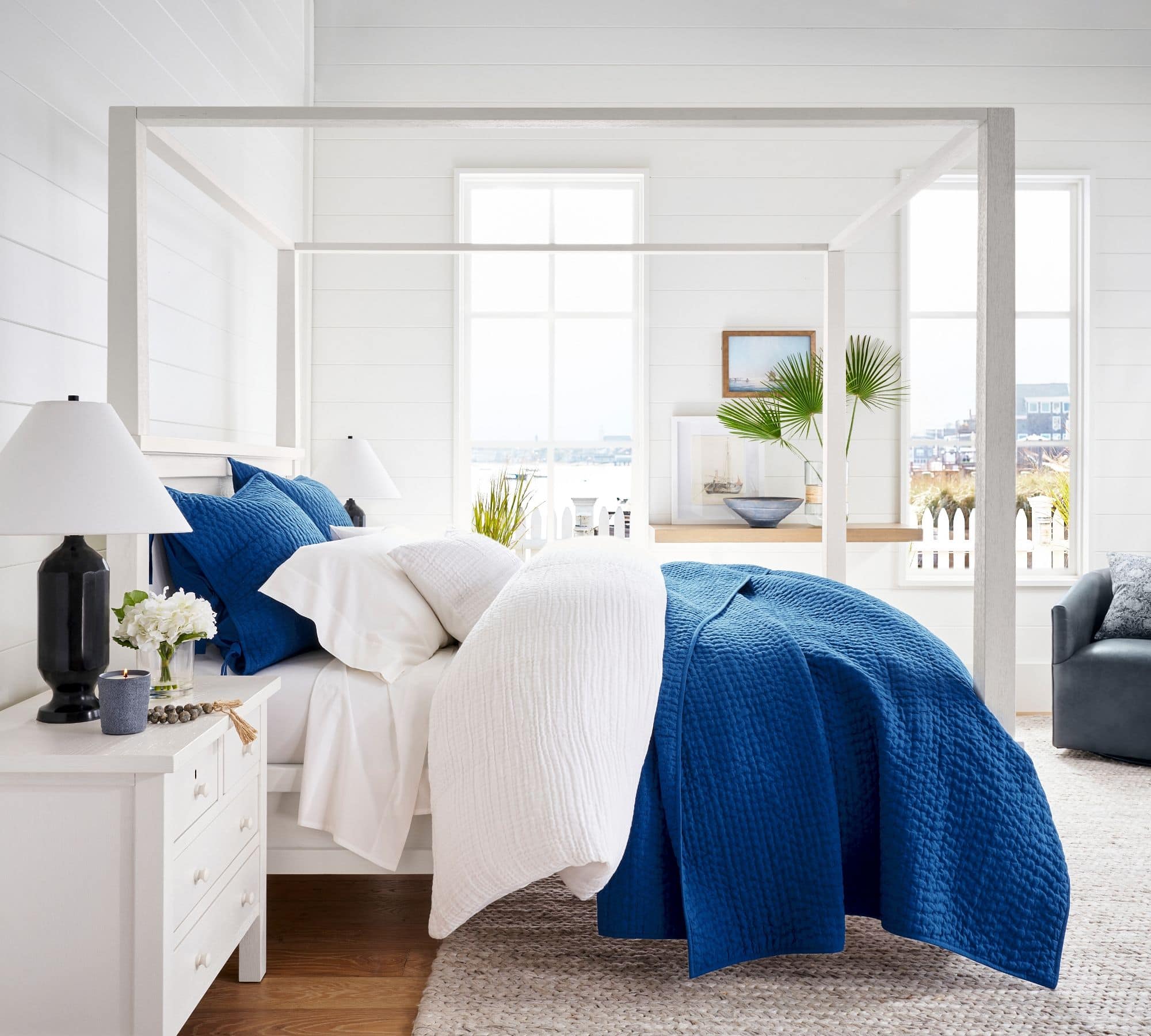 Bright blue coverlet and matching pillows with all white bedding. white furniture and a sisal rug
