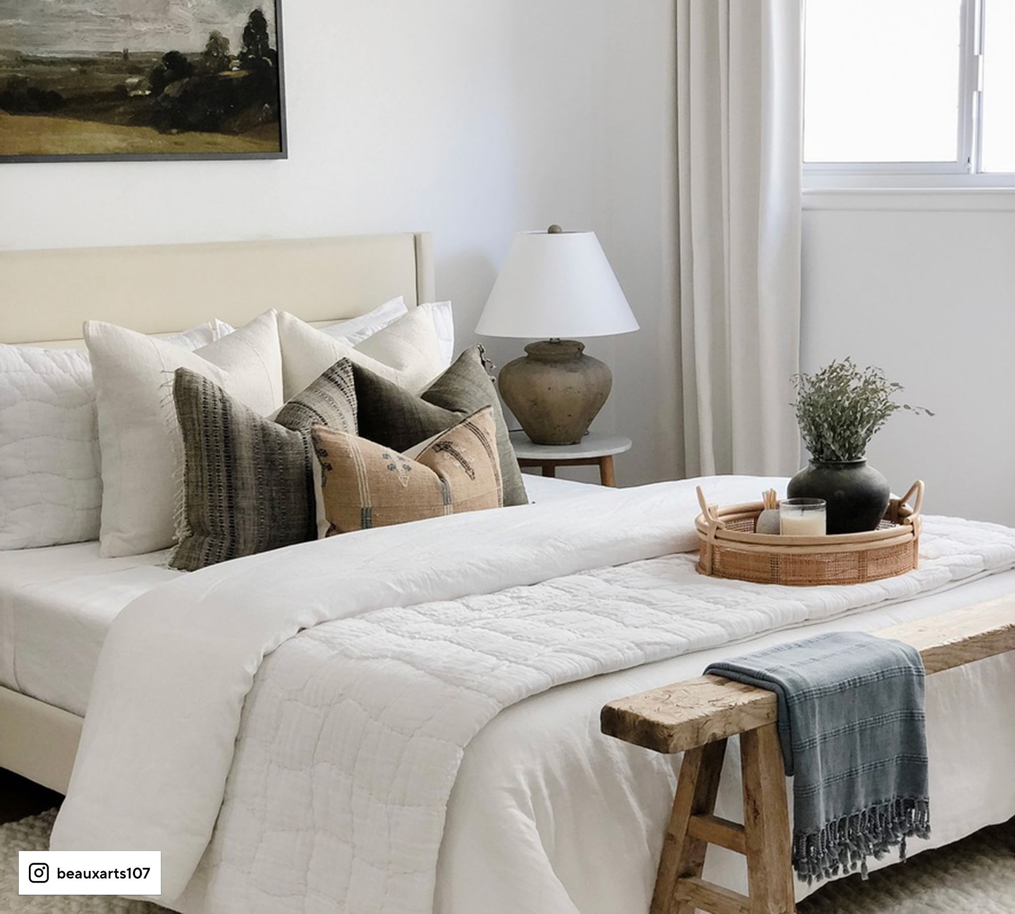white bedding, cream upholstered bed, wood bench at end of bed with blue throw blanket