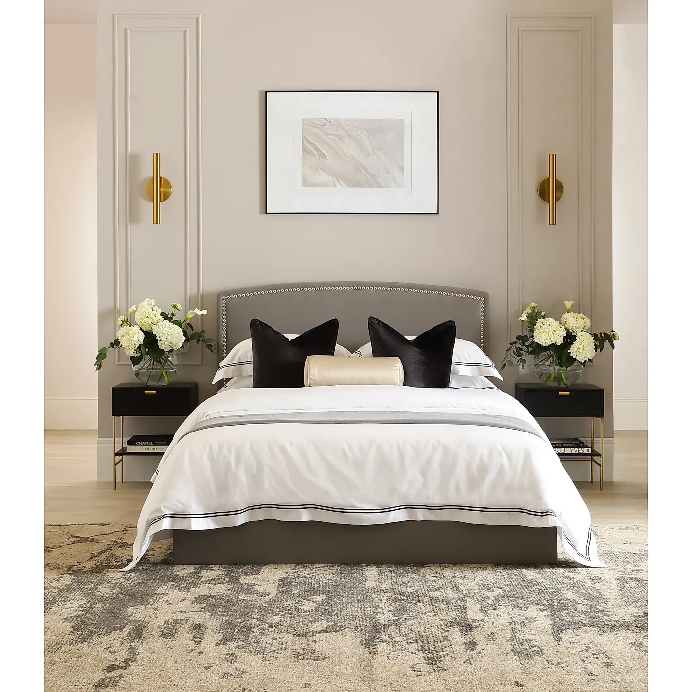 grey upholstered bed with nailheads, white hotel bedding, dark grey velvet pillows, cream satin bolster pillow.