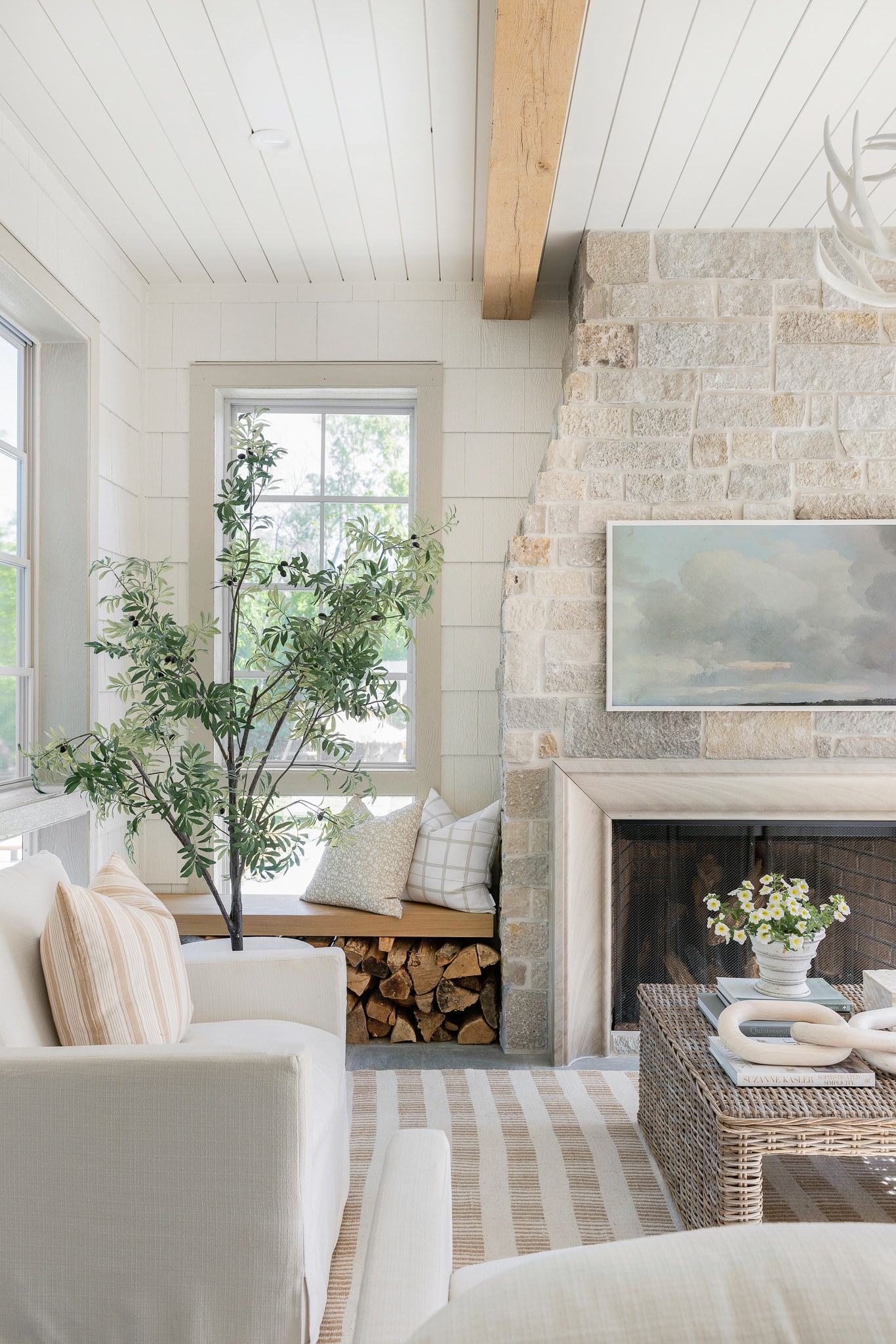 cream colored shingles inside a living room with a stone fireplace and buffalo print area rug in neutral shades.