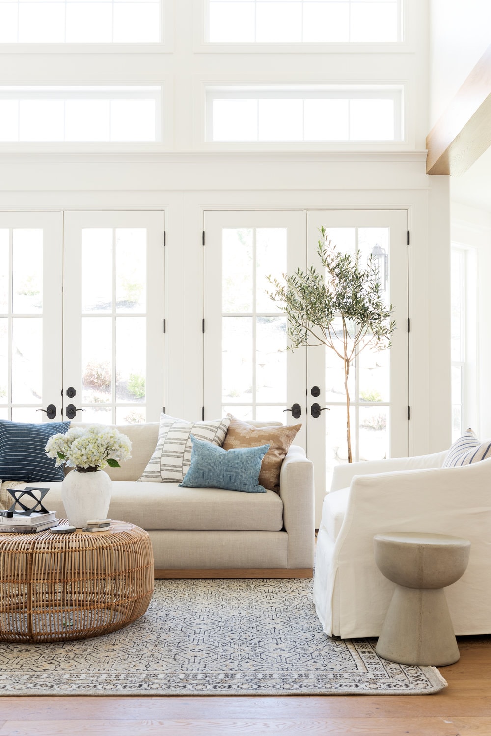 white painted living room with cream colored sofa, mix and match pillows, and a olive tree