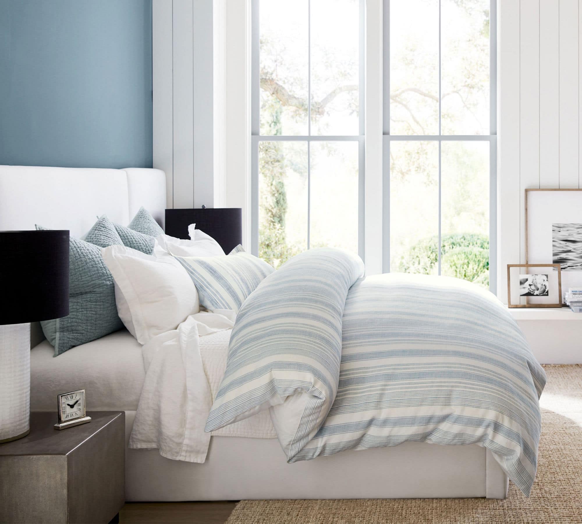 light blue comforter with white bedding on a white upholstered bed.