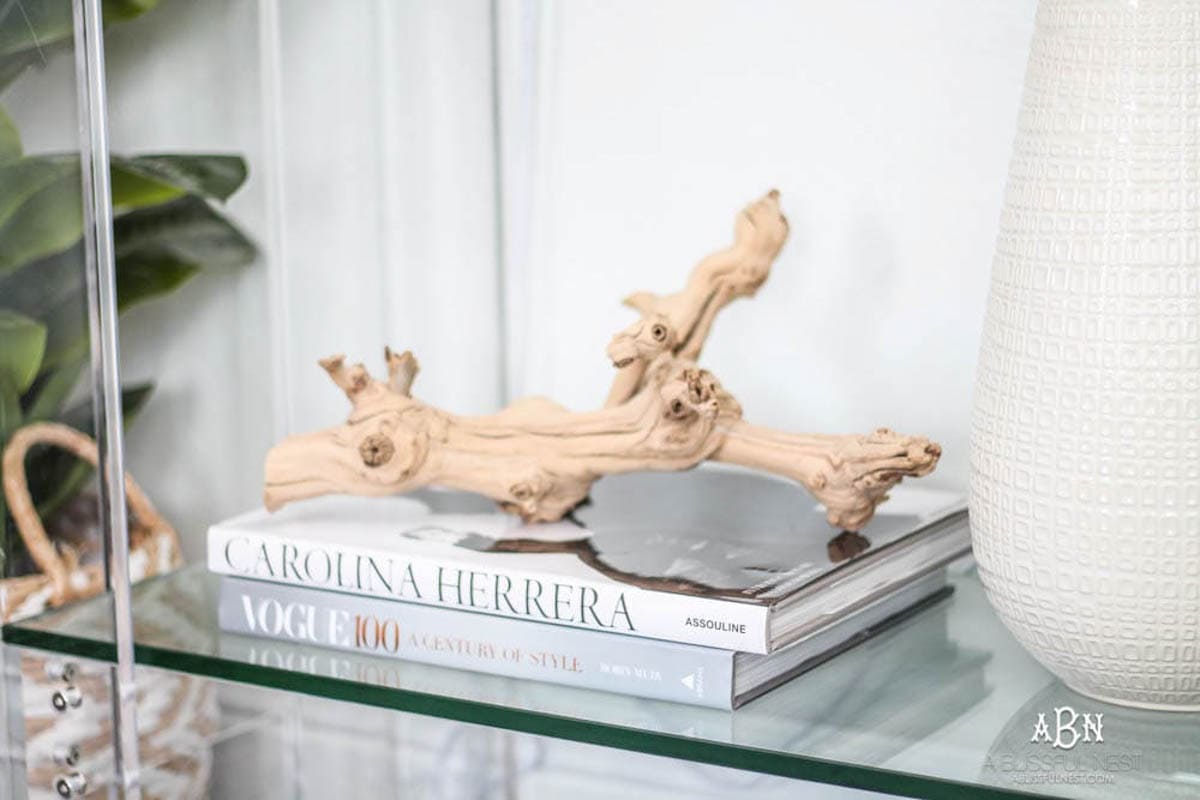 Rustic wood branch sitting on decorative books on the bottom shelf of a console table.
