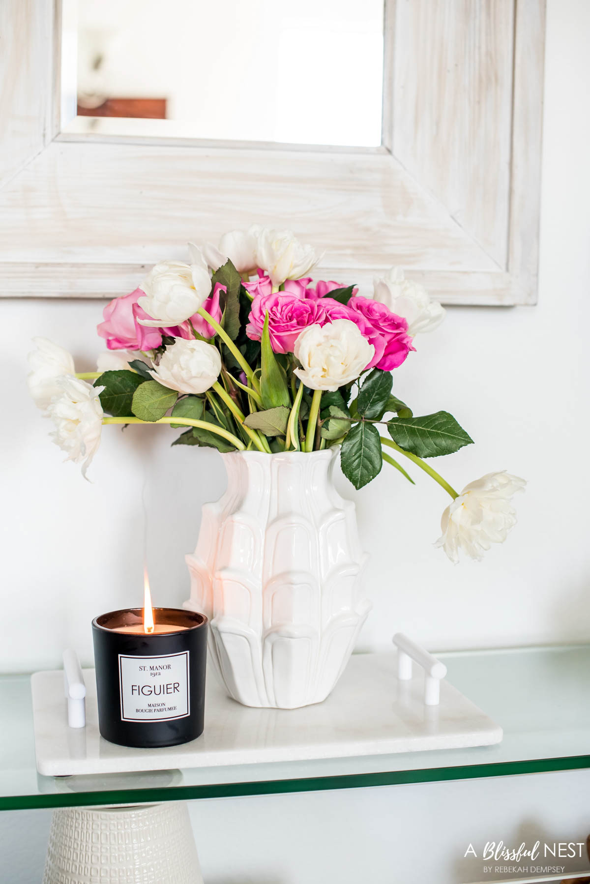 white vase filled with hot pink and white flowers on a white tray with a black candle on a console table