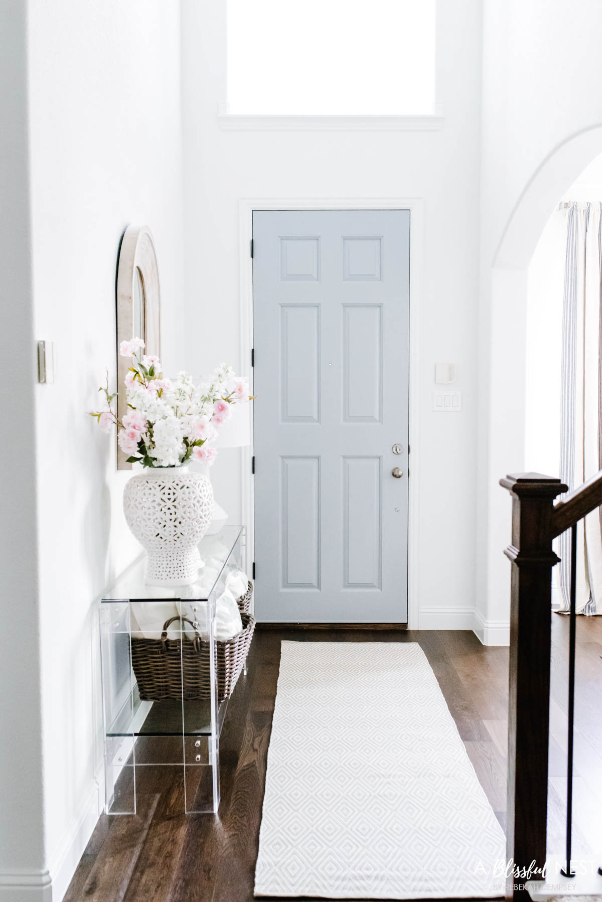 Light gray painted front door in an entryway with a lucite console table up against the wall.