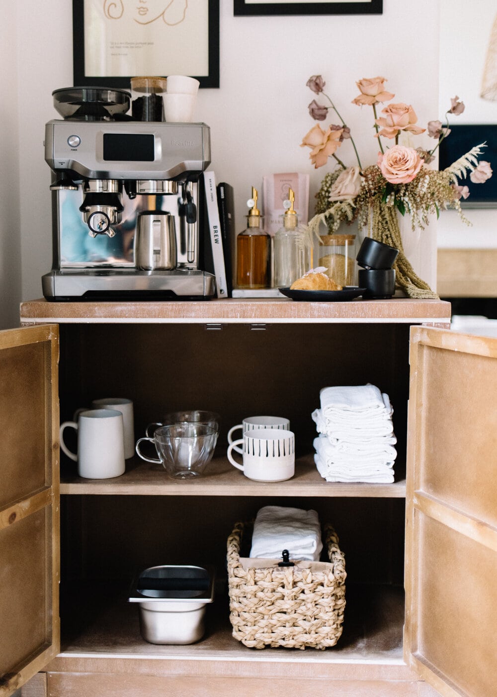a cabinet turned into a coffee cabinet with cups, towels, and an espresso machine