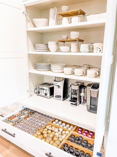Inside coffee cabinet with white plates and coffee mugs, drawer organized with coffee pods in sections.