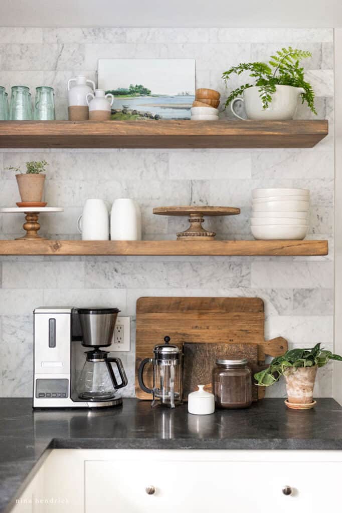 wood floating shelves in a kitchen with cake plates, coffee mugs, and bowls