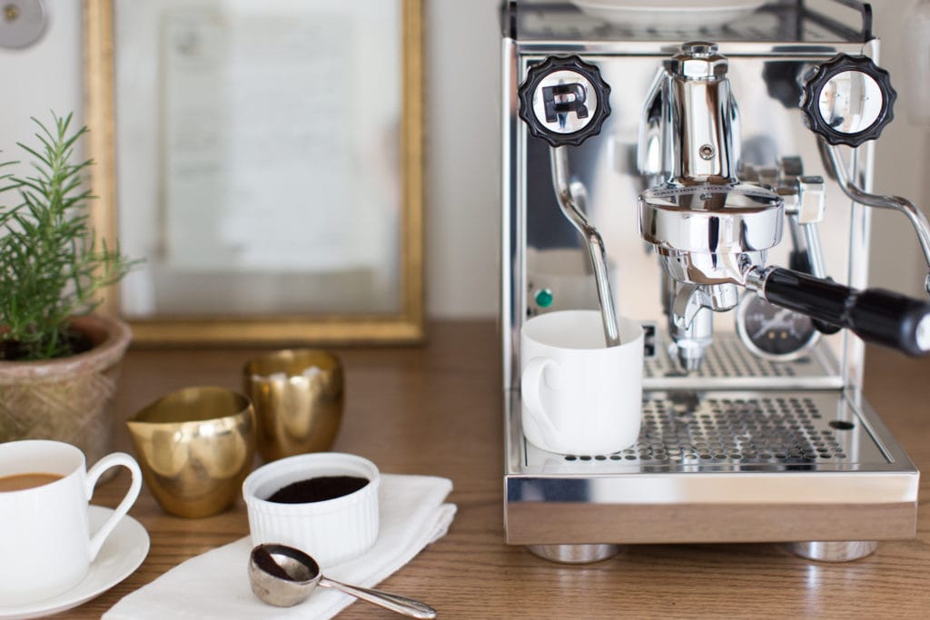 espresso machine with white coffee cups and gold containers for sugar and cream